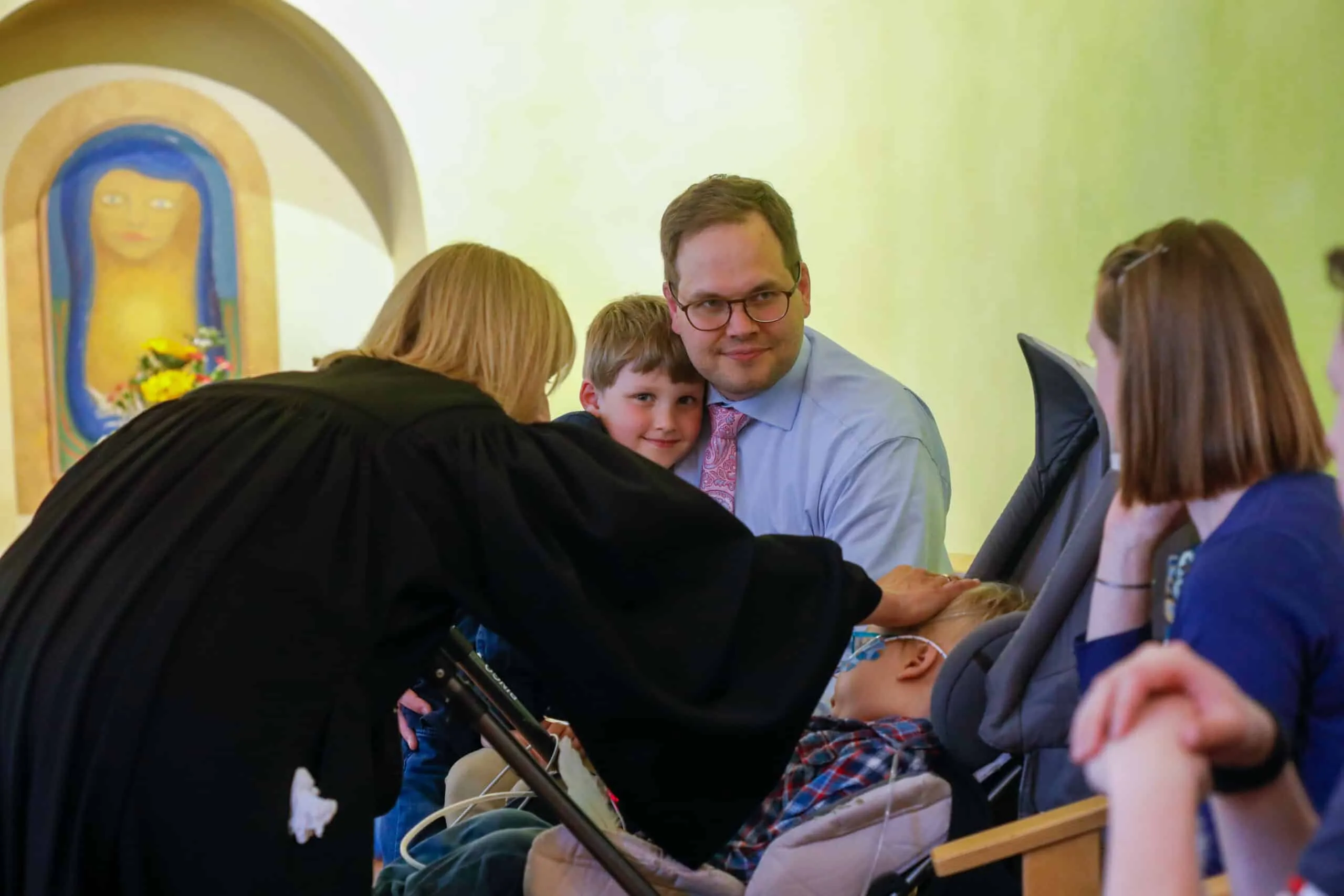 Die Pfarrerin legt dem Kind segnend die Hand auf den Kopf; Vater und Bruder sind ihm ganz nah.