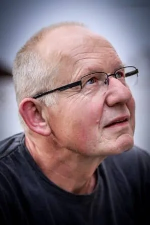 Porträt eines älteren Mannes mit Brille und kurzem grauem Haar, der nachdenklich nach oben blickt.