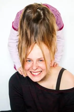 Lachende Frau, hinter der ein Kind steht und ihre langen Haare verspielt nach oben hält.