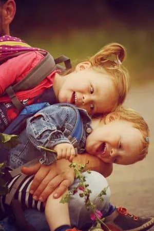 Zwei lachende Kleinkinder kuscheln ausgelassen auf dem Schoß eines Erwachsenen.