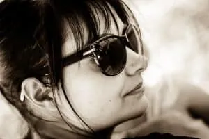 Sepia-Porträt einer Frau mit Sonnenbrille, die nachdenklich zur Seite blickt.